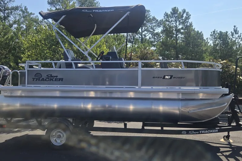 The Image of 2026 Sun Tracker Bass Buggy 18 DLX pontoon boat on trailer, surrounded by trees. - 0