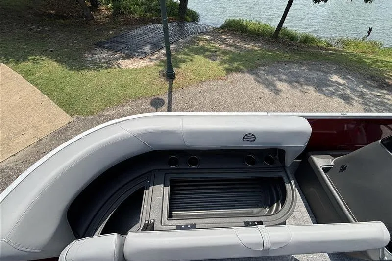 Slide: The Image of 2026 Sun Tracker Party Barge 16 DLX interior with seating and storage, near a lakeside. - 8