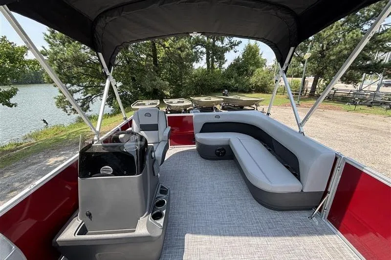 Slide: The Image of 2026 Sun Tracker Party Barge 16 DLX interior with seating and helm, near a scenic lake. - 10
