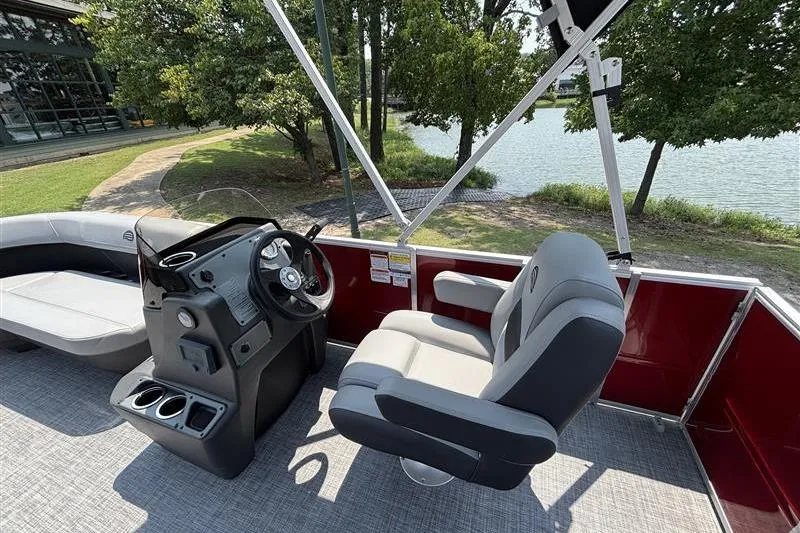 Slide: The Image of 2026 Sun Tracker Party Barge 16 DLX interior with steering console and seating by a lake. - 12