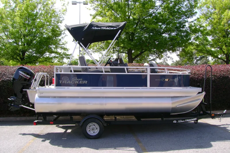 The Image of 2026 Sun Tracker Bass Buggy 16 XL Select pontoon boat on trailer, parked outdoors. - 0