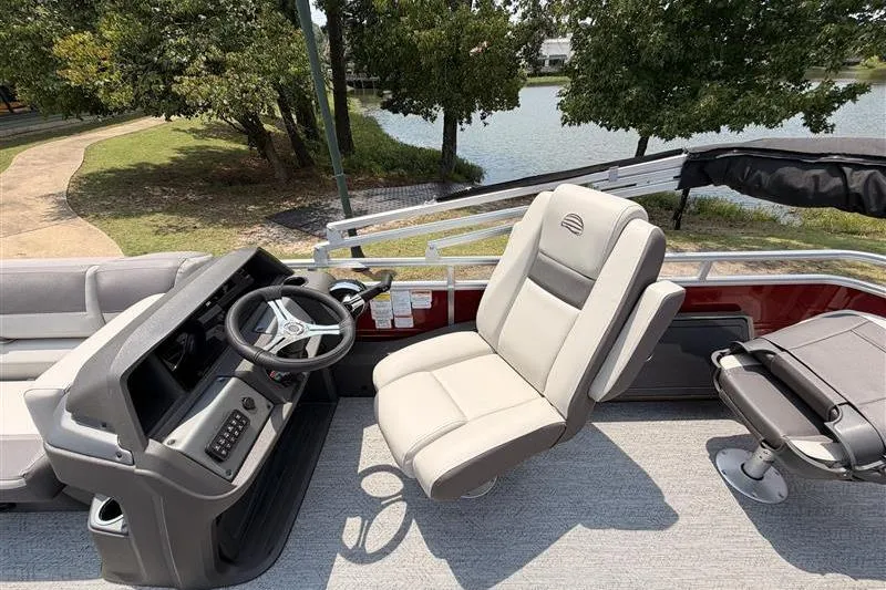 Slide: The Image of 2026 Sun Tracker Fishin' Barge 22 XP3 interior with steering console and seating by a lake. - 16