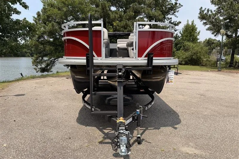 Slide: The Image of 2026 Sun Tracker Fishin' Barge 22 XP3 pontoon boat on trailer, parked near a lake. - 2
