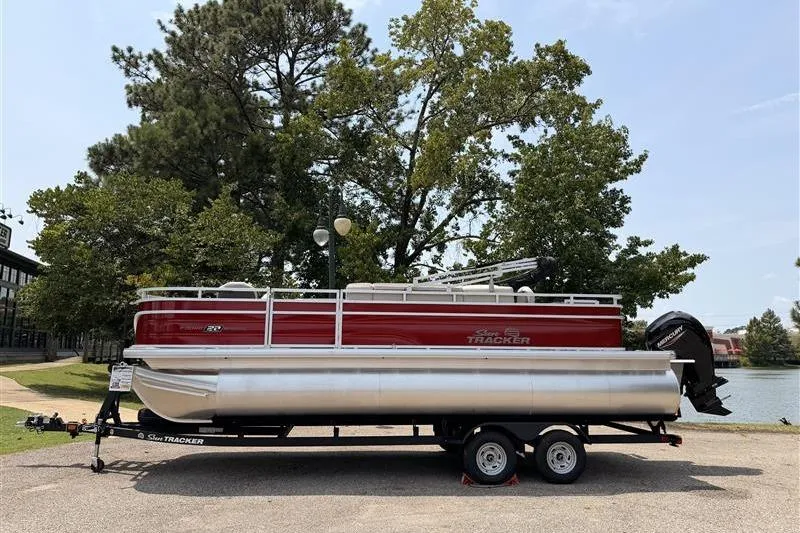 The Image of 2026 Sun Tracker Fishin' Barge 22 XP3 pontoon boat on trailer, parked near trees. - 0