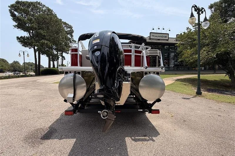 Slide: The Image of 2026 Sun Tracker Fishin' Barge 22 XP3 pontoon boat, rear view with motor, parked outdoors. - 3