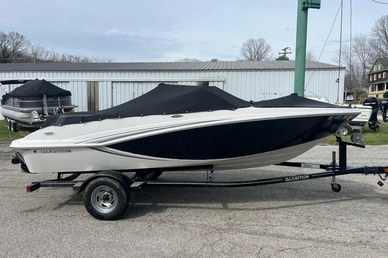 The Image of 2014 Glastron GT 185 boat on trailer, covered and parked outdoors. - 1