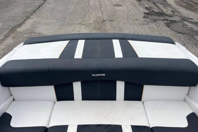 Slide: The Image of 2014 Glastron GT 185 boat interior with black and white seating on pavement background. - 10