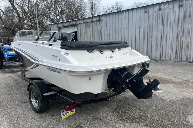 Slide: The Image of 2014 Glastron GT 185 boat on trailer, parked outdoors near a metal building. - 6