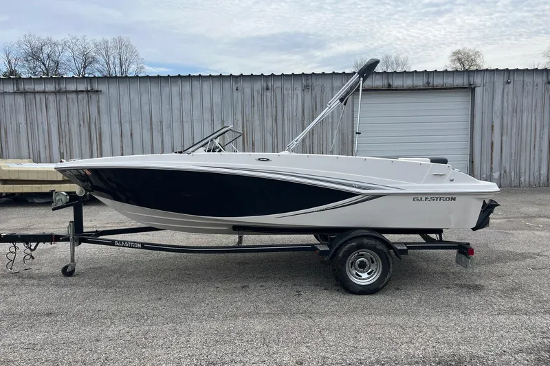 Slide: The Image of 2014 Glastron GT 185 boat on trailer, parked outdoors near a metal building. - 9