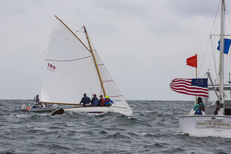 Slide: The Image of Sailboat Wianno Senior 2020 racing on choppy sea near a flag-bearing boat. - 6