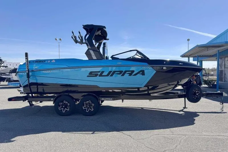 The Image of 2026 Supra SL boat in blue and black on a trailer, parked outdoors. - 0