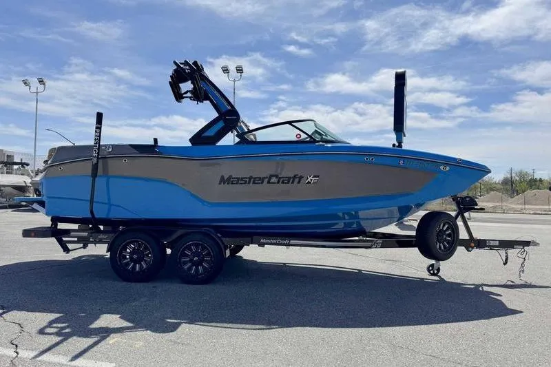 The Image of 2022 MasterCraft XT22 boat on trailer, blue and gray, parked outdoors under a clear sky. - 0