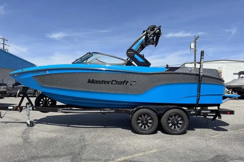 Slide: The Image of 2022 MasterCraft XT22 boat in blue on a trailer, parked outdoors. - 14