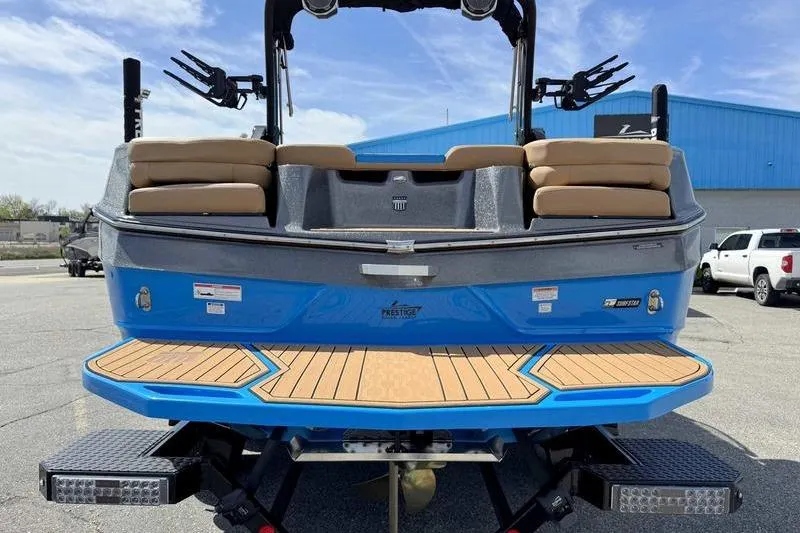 Slide: The Image of 2022 MasterCraft XT22 boat, blue exterior, tan seating, parked outdoors. - 2