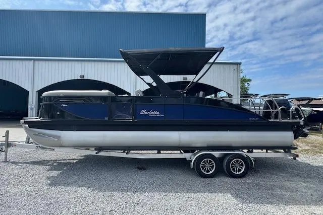 Slide: The Image of 2026 Barletta Cabrio 24UE pontoon boat on trailer, parked outside a warehouse. - 6