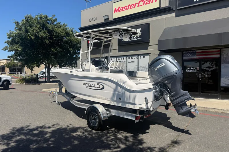 Slide: The Image of 2025 Robalo R180 Center Console boat with Yamaha engine on trailer, parked outside dealership. - 2