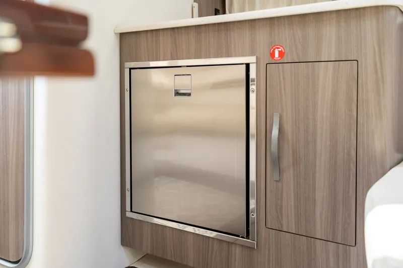 Slide: The Image of Galley area of the 2019 Regal 33 Express with stainless steel fridge and wooden cabinetry. - 24