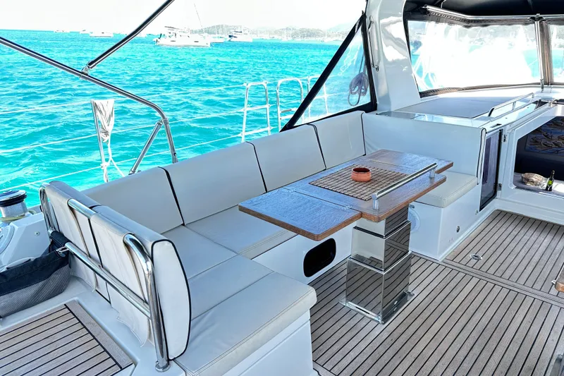 Slide: The Image of Luxurious 2019 Beneteau Oceanis Yacht 62 deck with seating and table, overlooking turquoise waters. - 18