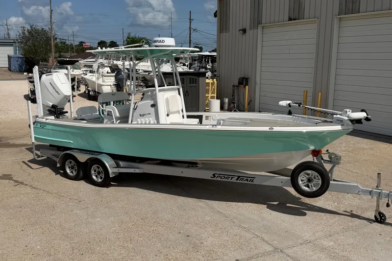 The Image of 2024 BlackJack 256 Bay boat on trailer, mint green hull, parked outside a warehouse. - 1