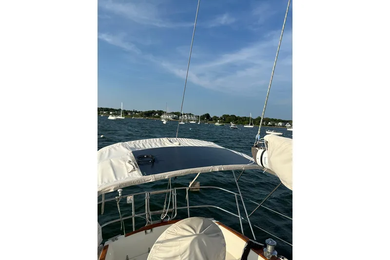 Slide: The Image of 1984 Sabre 38 sailboat on water, clear sky, distant shoreline, and moored boats. - 63