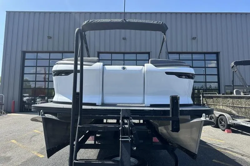 Slide: The Image of 2024 Manitou 24 X-Plode Cruise SHP pontoon boat on trailer, parked outside a warehouse. - 14