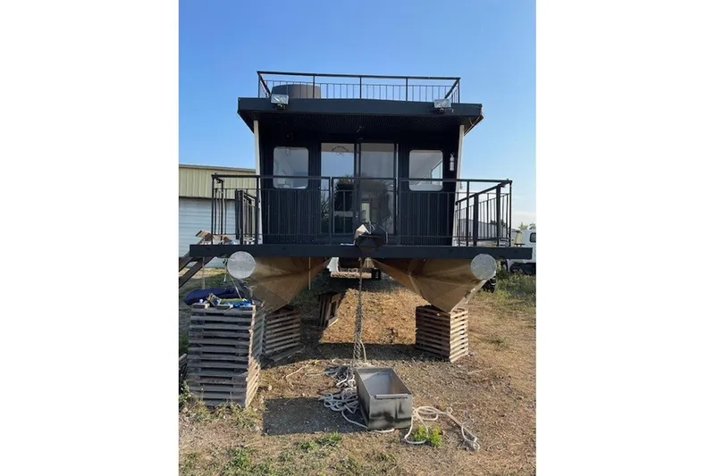 Slide: The Image of 1985 Three Buoys houseboat on land, elevated on blocks, with a modern black exterior. - 2