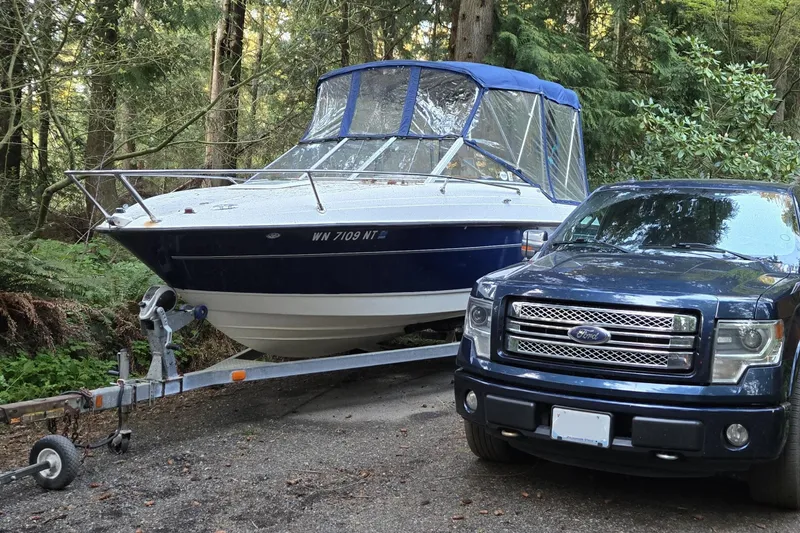 Slide: The Image of 2006 Bayliner 192 Discovery Cuddy on trailer beside a parked truck in a wooded area. - 2
