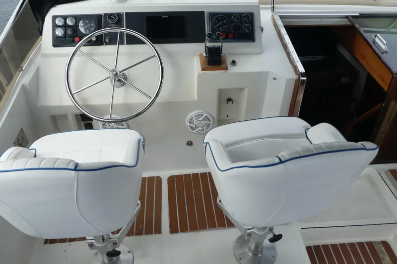 Slide: The Image of 1989 Angel Pilothouse boat helm with steering wheel and white captain chairs. - 46