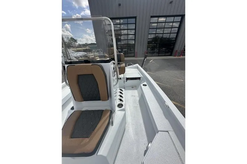 Slide: The Image of 2025 Xpress H20B Bay boat interior with tan and black seating, parked outside a building. - 18