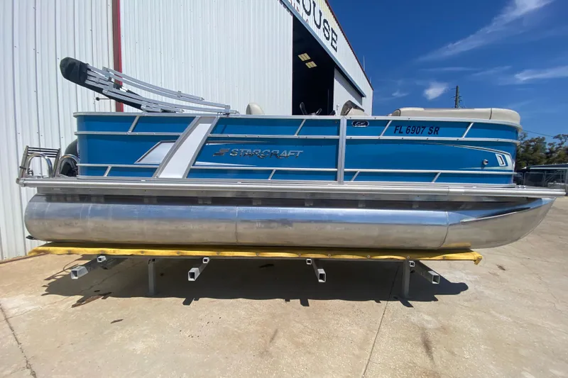 The Image of 2020 Star Craft 20 DLX pontoon boat in blue, parked outside a warehouse. - 1