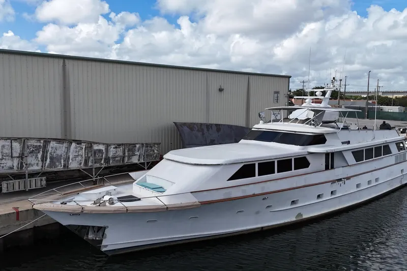 Slide: The Image of Luxury yacht Denison 109, 1990 model, docked beside industrial building under cloudy sky. - 10