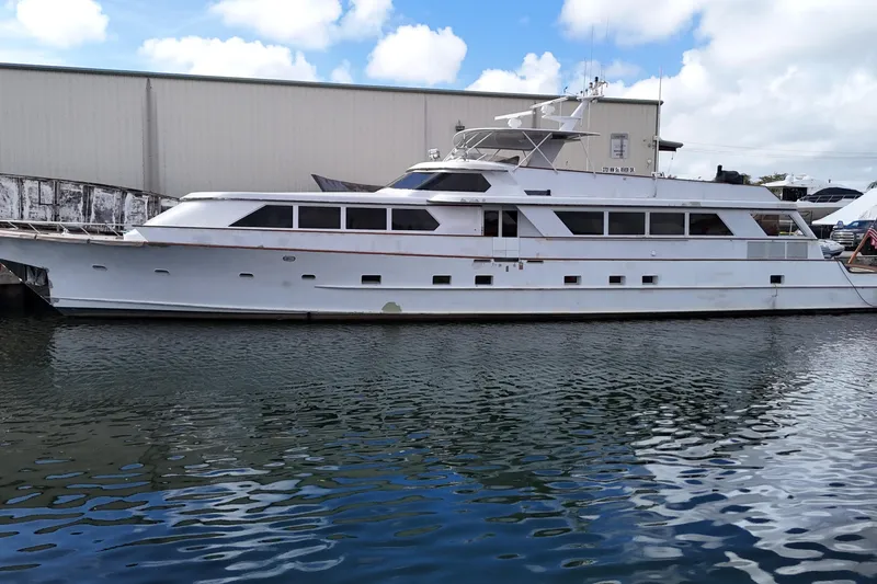 Slide: The Image of 1990 Denison 109 yacht docked by a warehouse under a partly cloudy sky. - 2