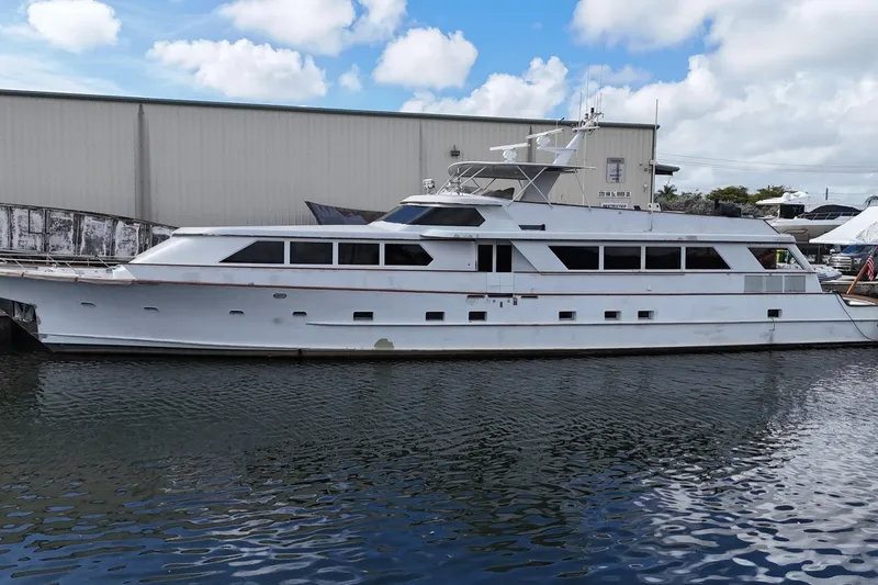 Slide: The Image of 1990 Denison 109 yacht docked by a warehouse under a partly cloudy sky. - 3