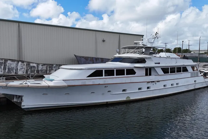 Slide: The Image of Luxury 1990 Denison 109 yacht docked by a warehouse under a cloudy sky. - 9