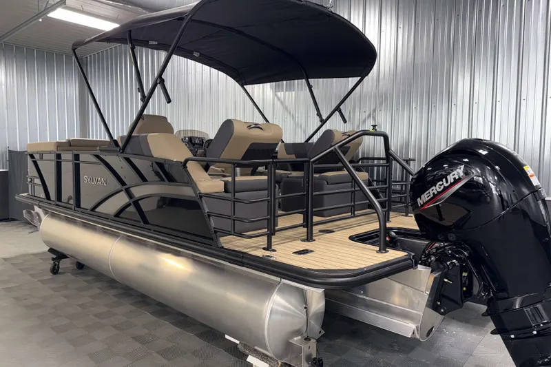 Slide: The Image of 2026 Sylvan L1 LZ pontoon boat with Mercury engine in a metal-walled showroom. - 29