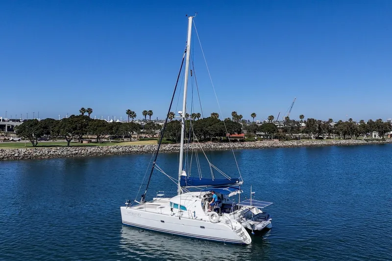 Slide: The Image of 2004 Lagoon 380 catamaran sailing near a scenic coastline under a clear blue sky. - 31