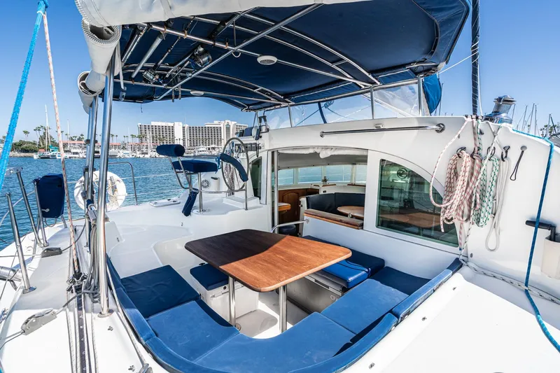 Slide: The Image of Lagoon 380 catamaran cockpit with blue seating, wooden table, and marina view, 2004 model. - 32