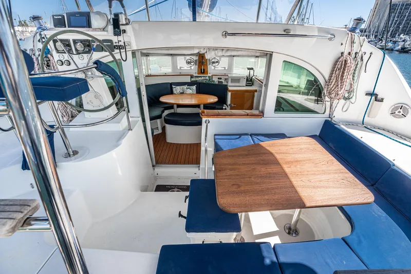 Slide: The Image of Cockpit and interior of 2004 Lagoon 380 catamaran with blue seating and wooden table. - 42