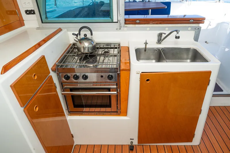 Slide: The Image of Compact kitchen in a 2004 Lagoon 380 yacht with stove, sink, and wooden cabinetry. - 50