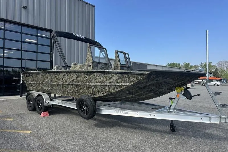 The Image of 2025 SeaArk Predator 300 AK boat on trailer, camo design, parked outside industrial building. - 1