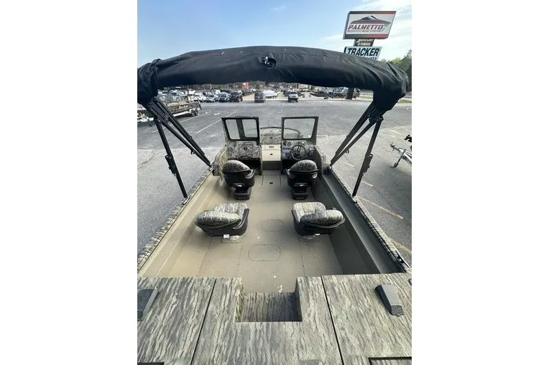 Slide: The Image of 2025 SeaArk Predator 300 AK boat interior with seating and canopy, parked outdoors. - 15