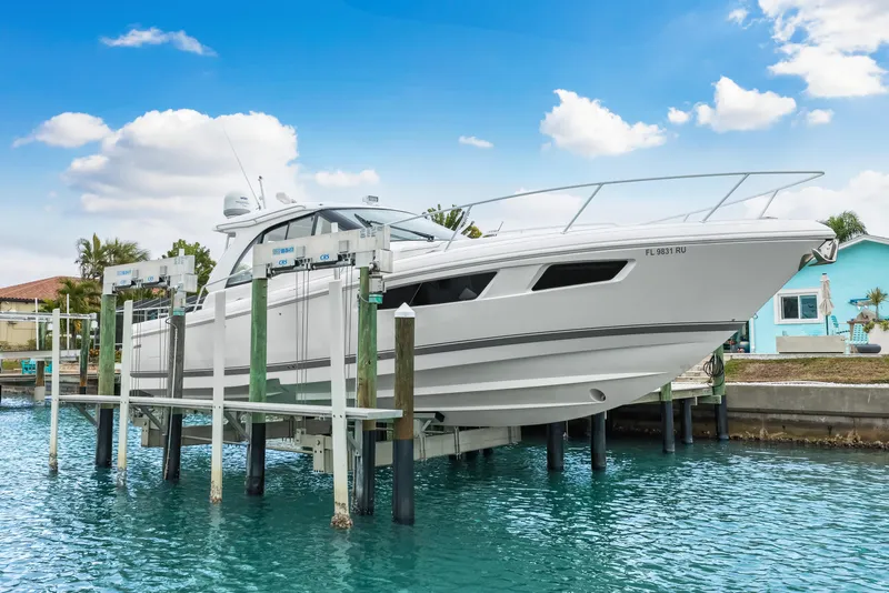 Slide: The Image of 2019 Intrepid 410 Evolution yacht on lift, docked by waterfront homes under blue sky. - 2