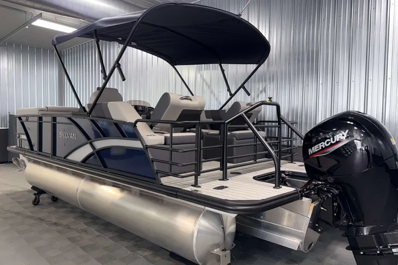 Slide: The Image of 2026 Sylvan L1 LZ pontoon boat with Mercury outboard motor in a metal-walled showroom. - 26
