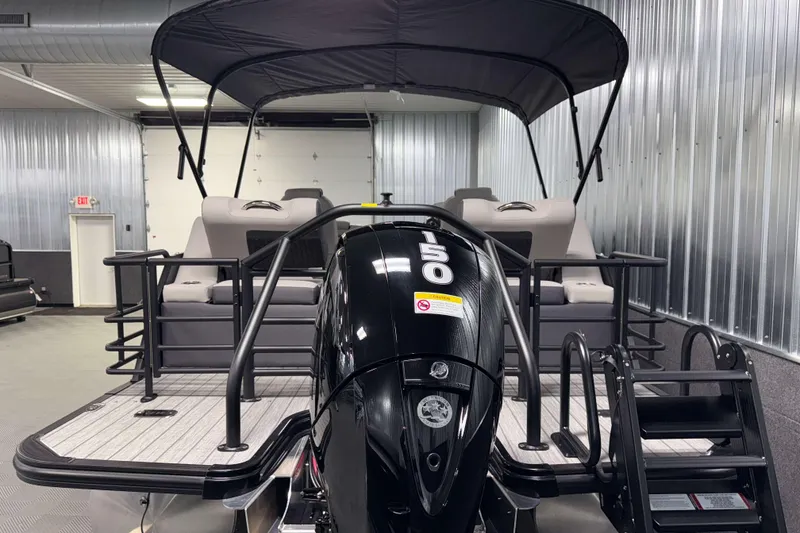 Slide: The Image of 2026 Sylvan L1 LZ pontoon boat with 150 HP engine in a metal-walled showroom. - 31