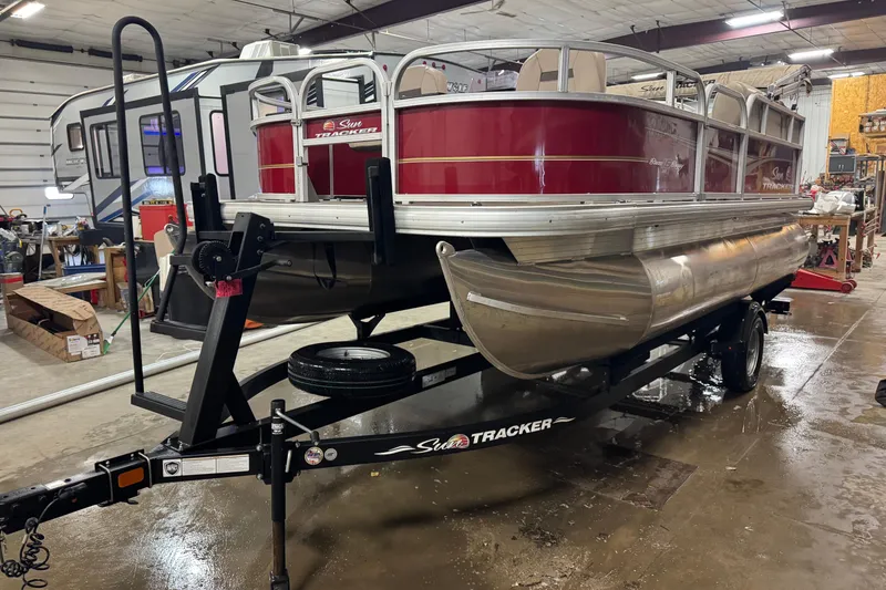 The Image of 2024 Sun Tracker Bass Buggy 16 XL Select pontoon boat on trailer in garage. - 0