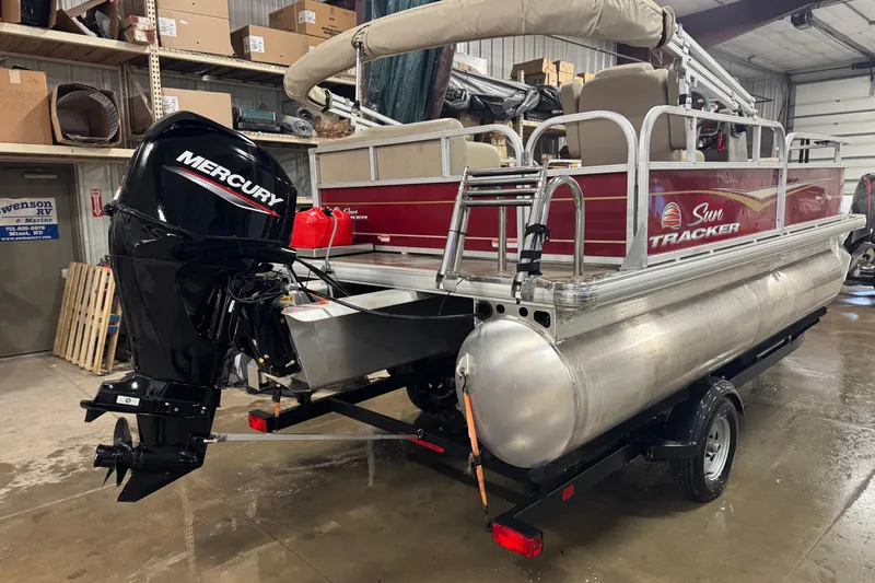 Slide: The Image of 2024 Sun Tracker Bass Buggy 16 XL Select pontoon boat with Mercury outboard motor in a showroom. - 2