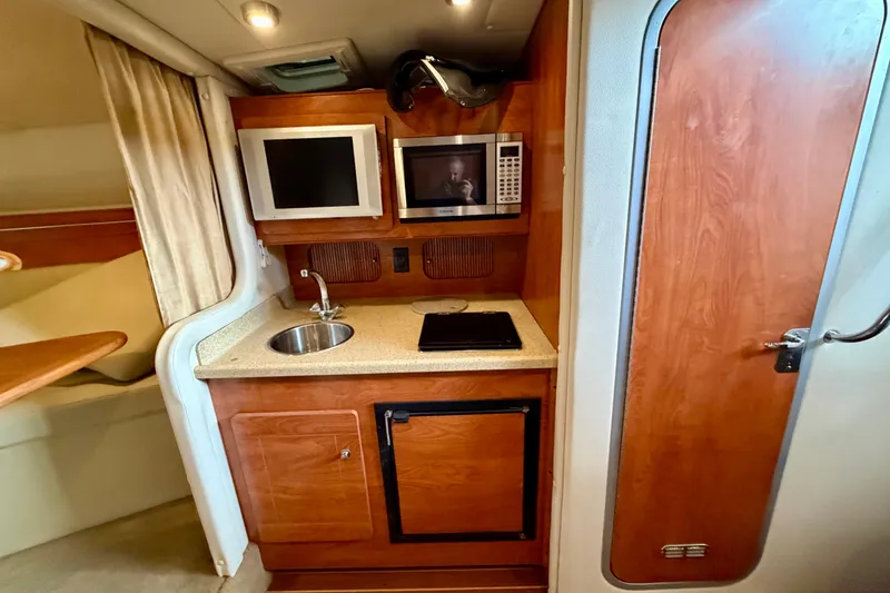 Slide: The Image of 2006 Rinker 300 Express Cruiser interior kitchen with sink, microwave, and wooden cabinetry. - 25