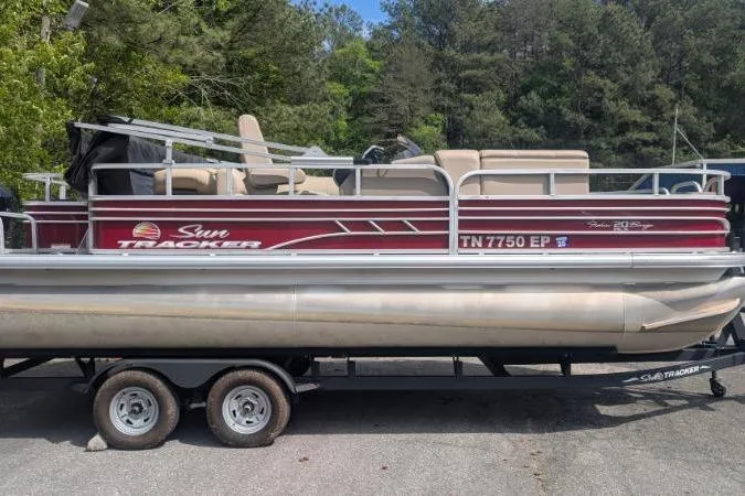 The Image of 2022 Sun Tracker Fishin' Barge 20 DLX pontoon boat on trailer, surrounded by trees. - 1