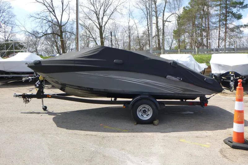 The Image of 2015 Yamaha Boats SX192 covered on trailer, parked outdoors with trees in background. - 1