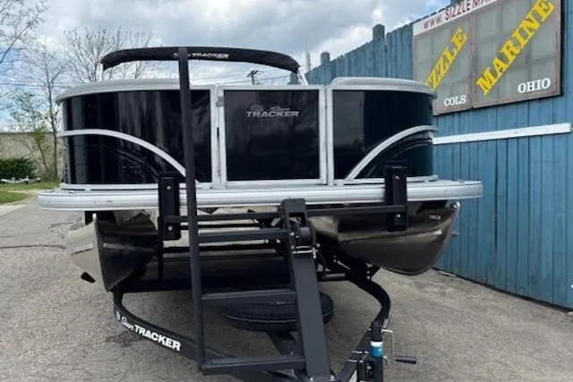 Slide: The Image of 2026 Sun Tracker Party Barge 20 DLX pontoon boat on trailer, parked near blue fence. - 2